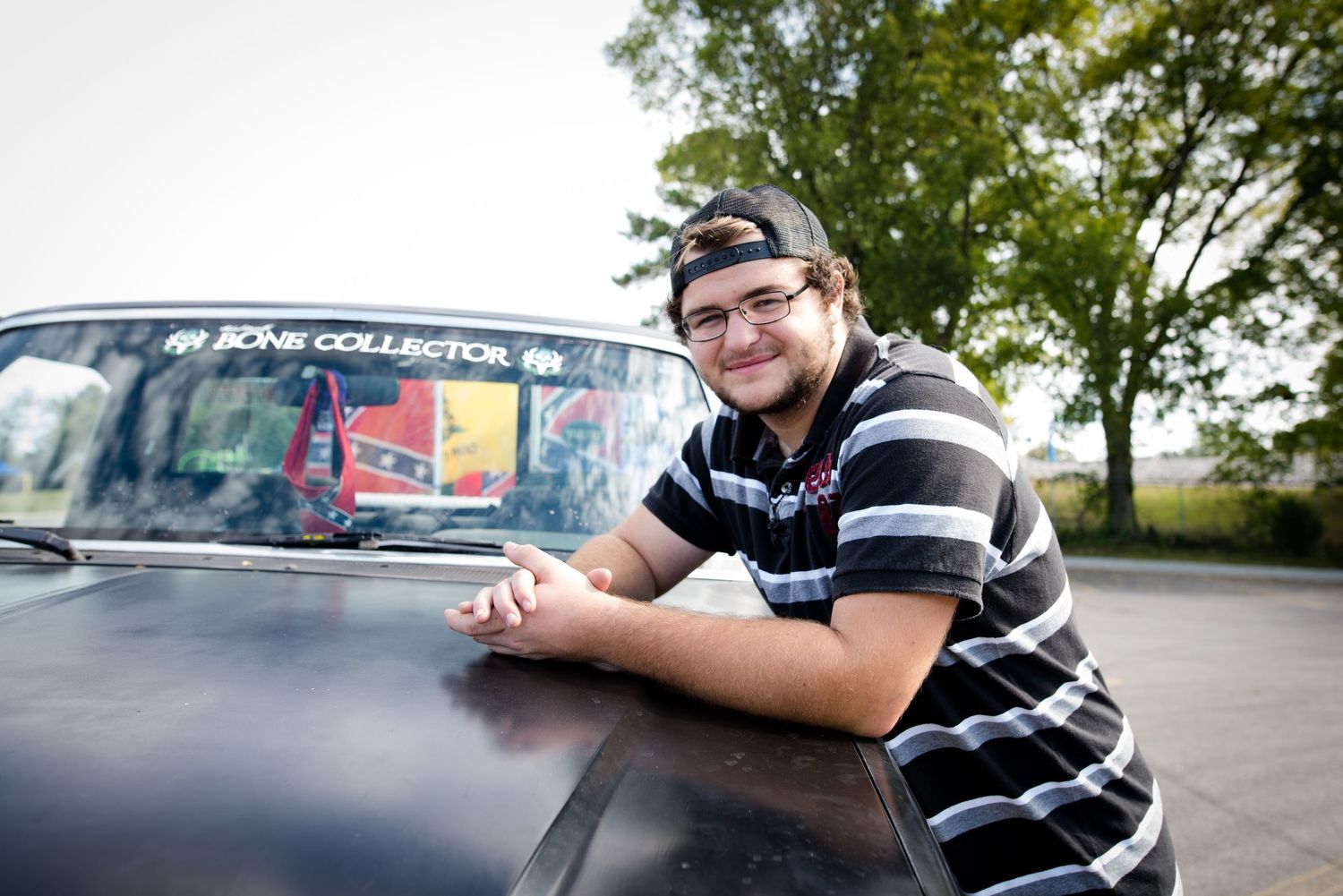 Person leaning on black car hood in striped shirt.