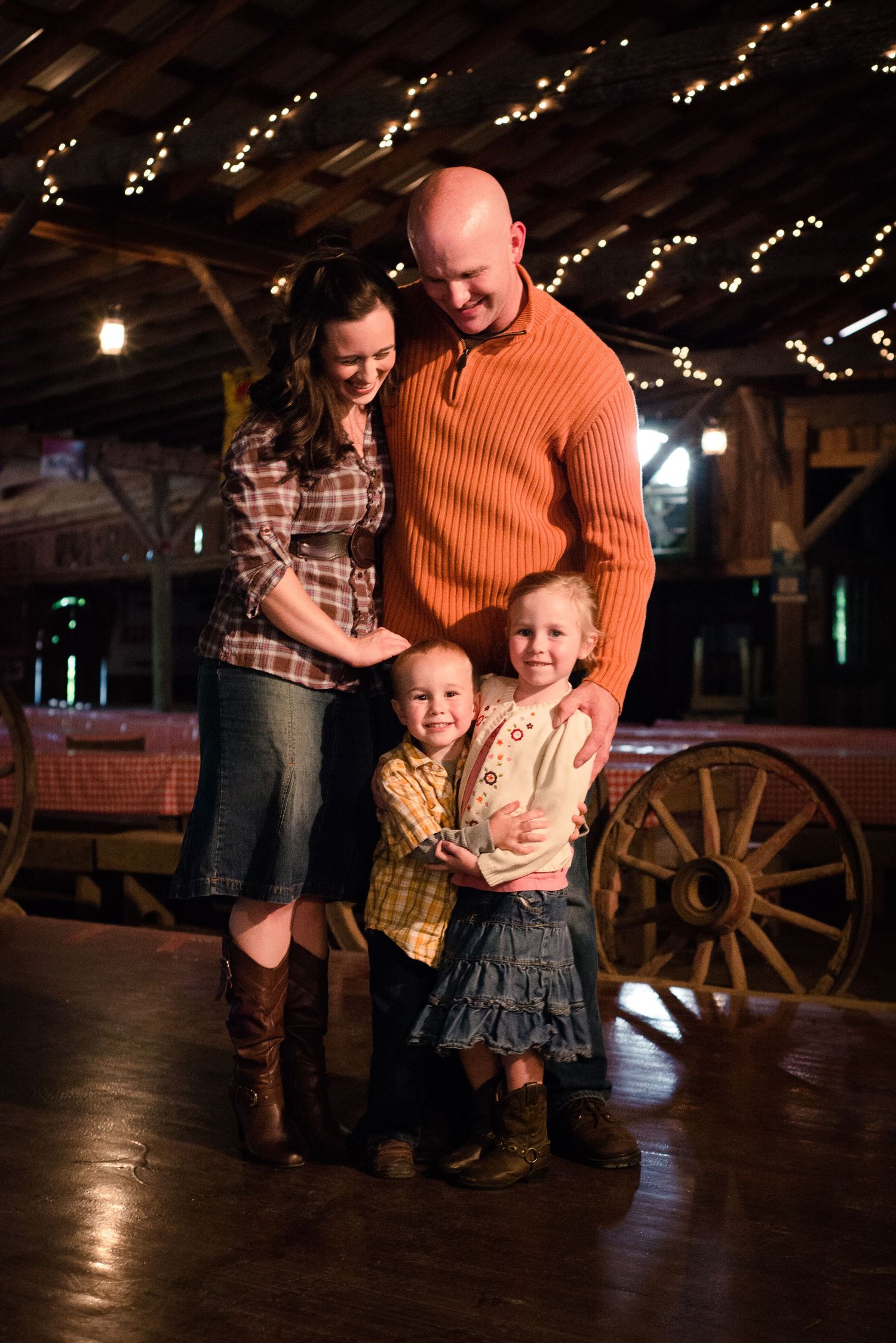 A family shares joyful moments together in a rustic barn setting illuminated by warm string lights.