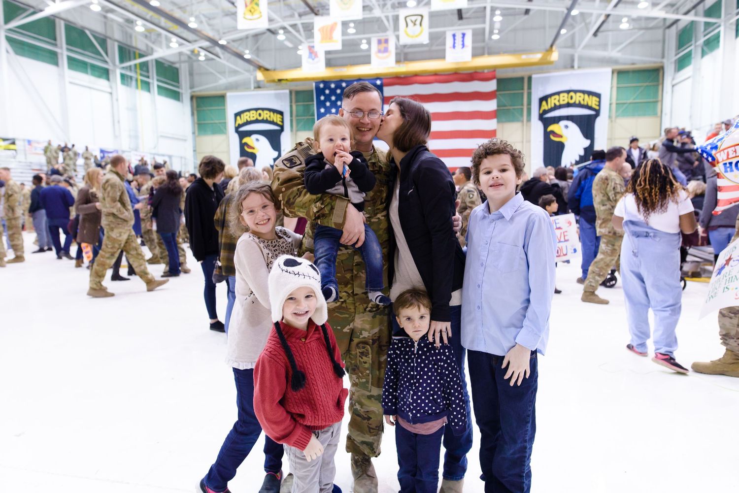 Large indoor gathering with American flag and military patches displayed on the wall. Fort Campbell KY homecoming