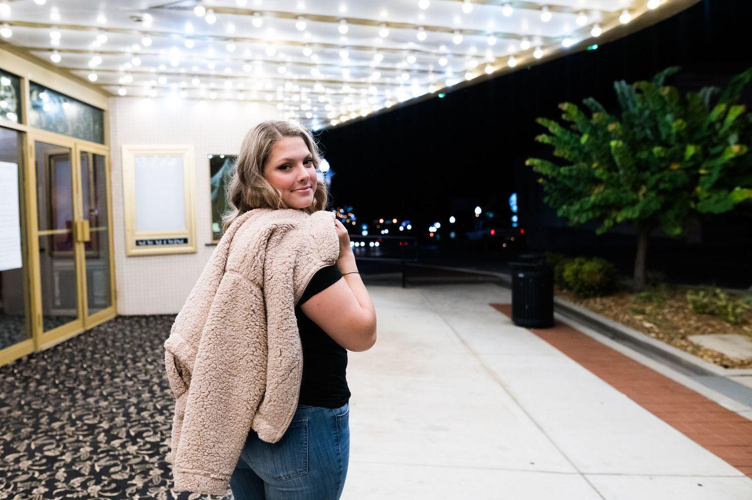 A person wearing a beige vest stands outside a building entrance at night.