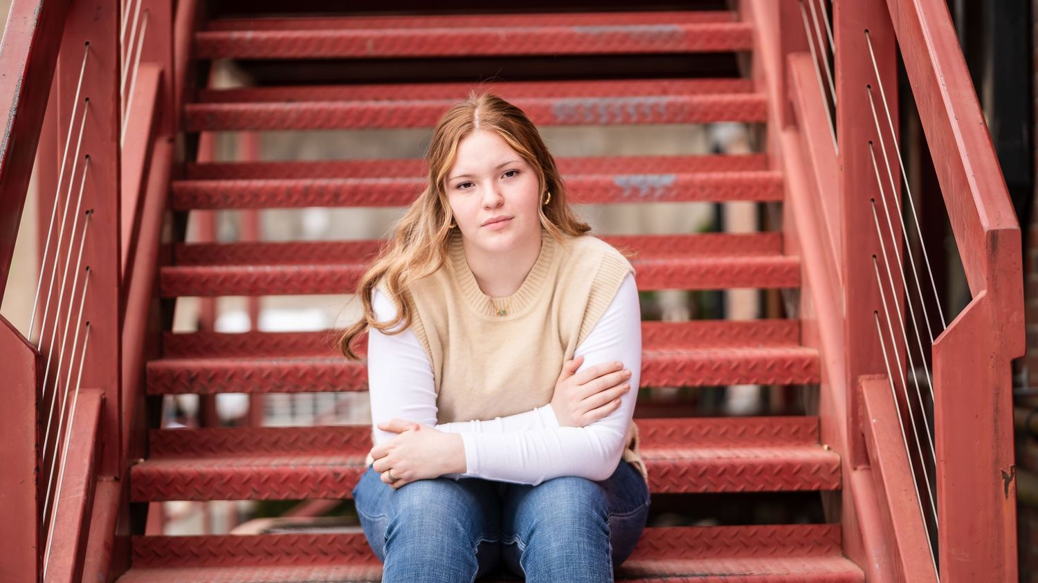 A casual senior portrait on red metal stairs with natural lighting.