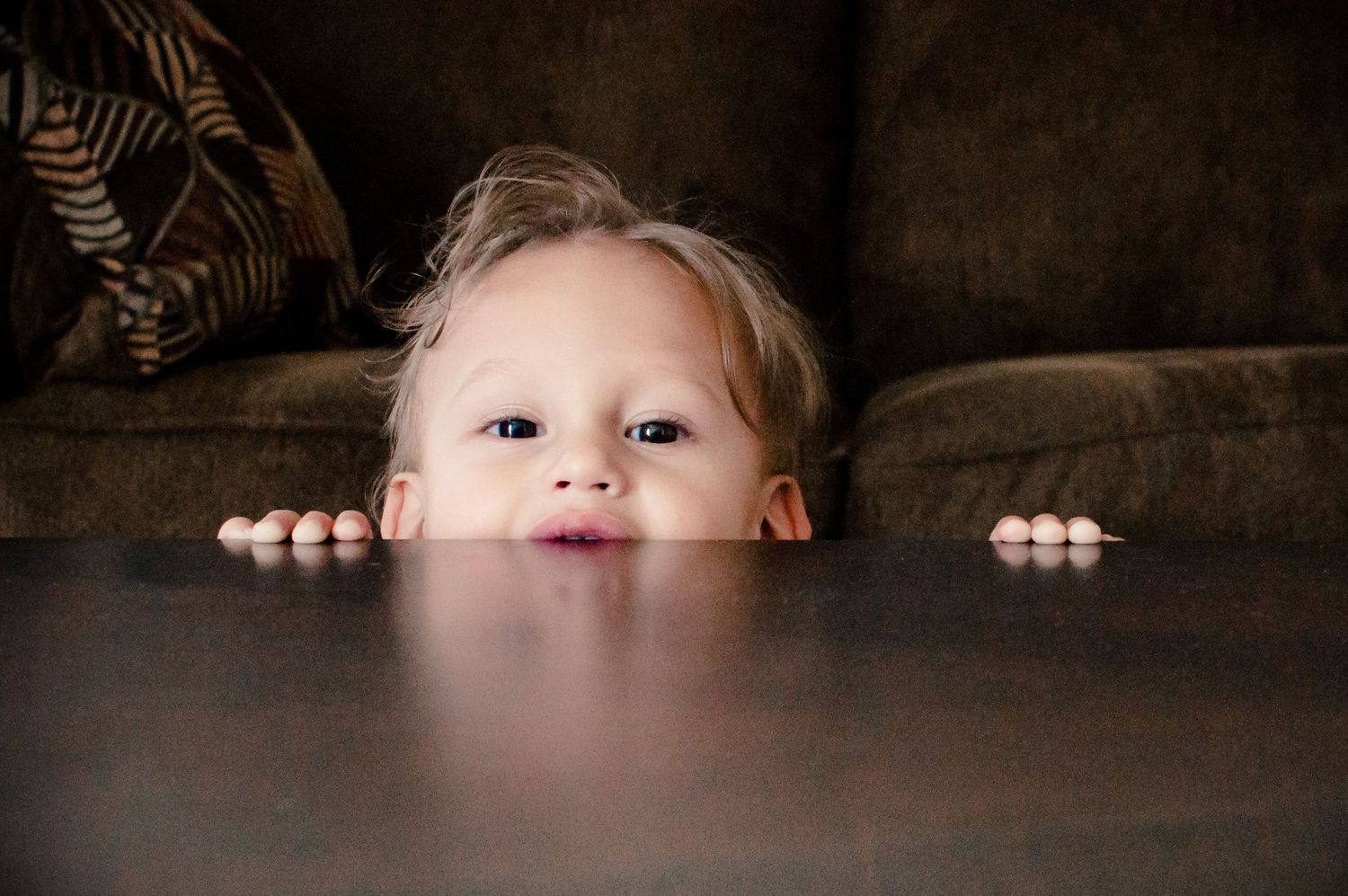 Child peeking over edge of table with playful expression.