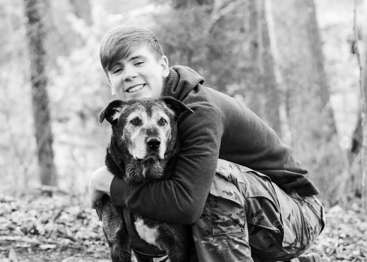 Black and white senior portrait of a boy with his dog in autumn leaves.
