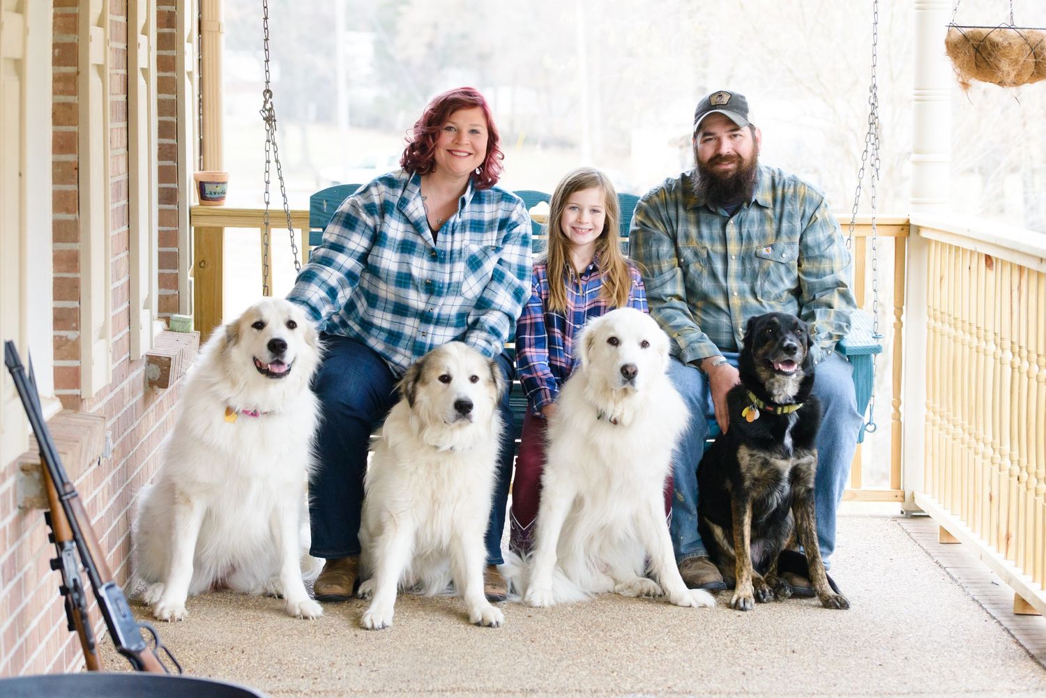 Family portrait on porch with multiple white fluffy dogs sitting in a row.