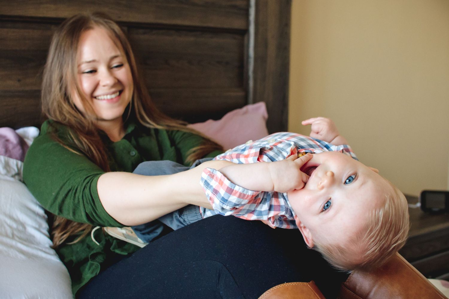 Playful moment between parent and child on bed with green sweater.