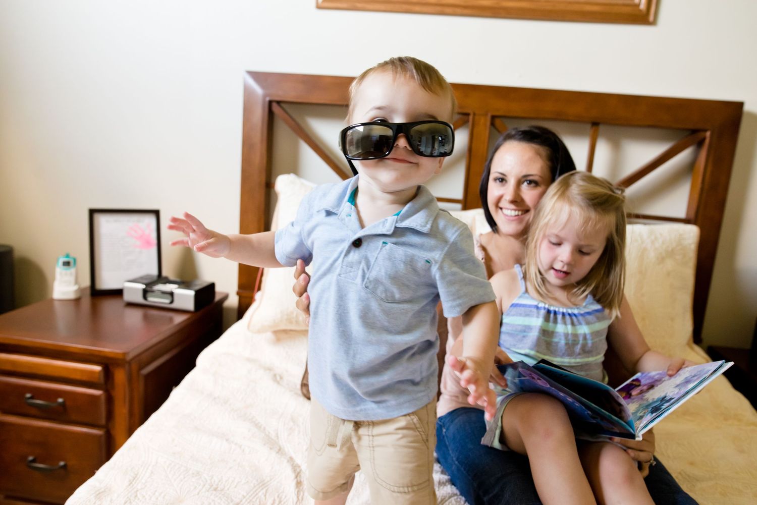 Playful scene on bed with child wearing sunglasses and reading time.