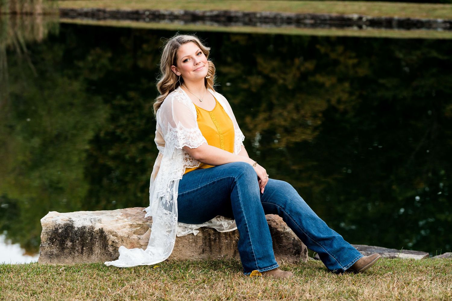 Casual outdoor photoshoot near a serene pond with natural landscape elements.