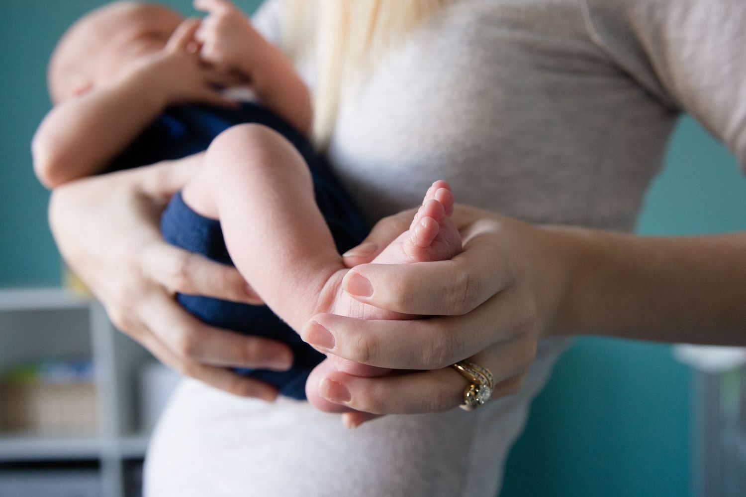 Close-up of hands holding tiny baby feet wearing navy clothing.