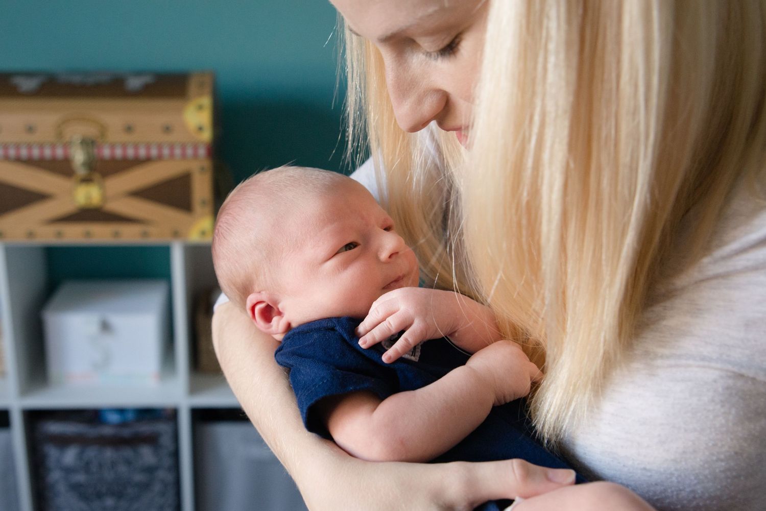 A tender moment between parent and newborn baby in a navy blue onesie against a teal wall.