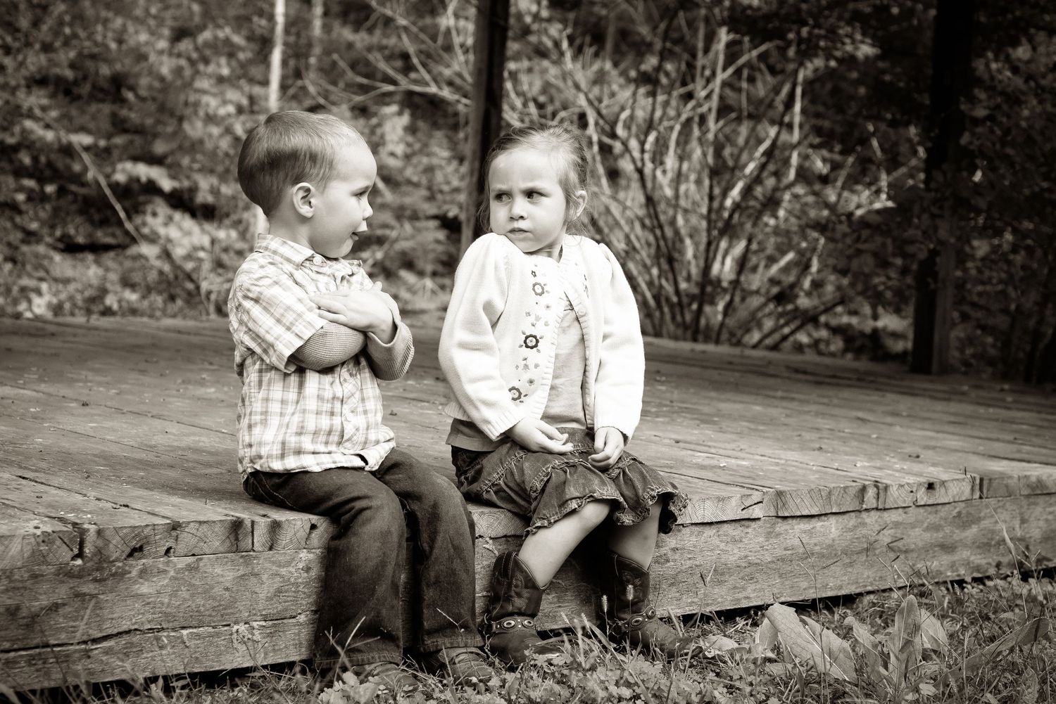 Vintage black and white photograph of two young children sitting together on a wooden log outdoors.