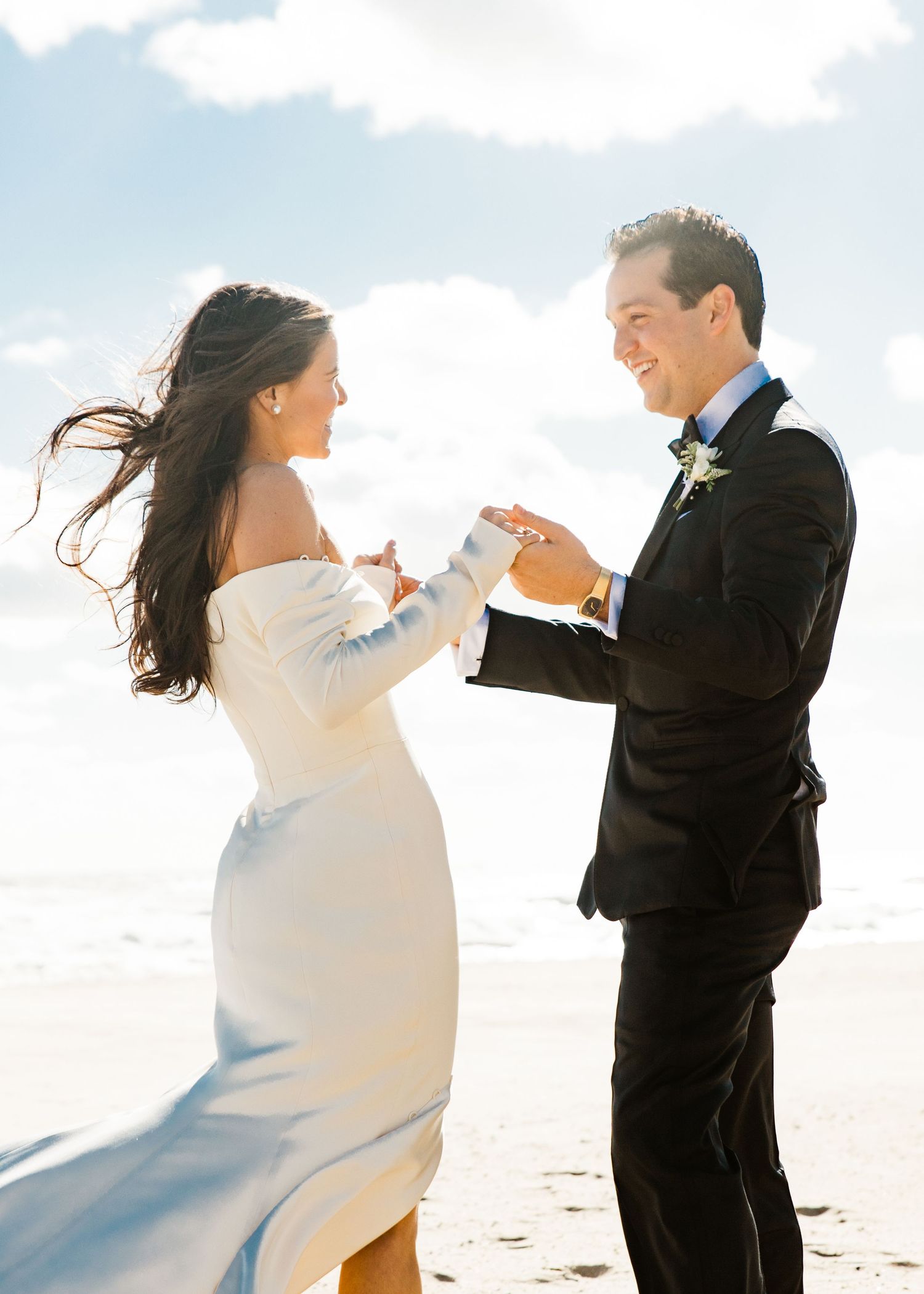 Elegant bride and groom holding hands and dancing together on a sandy beach wedding.