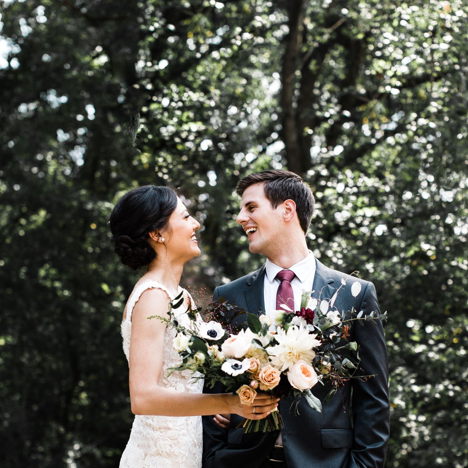 Bride and groom smiling at each other in lush green outdoor wedding portrait.