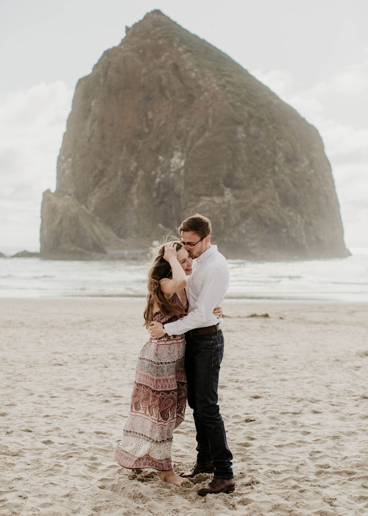 Couple slow dancing on Cannon Beach with majestic Haystack Rock towering in the misty background.