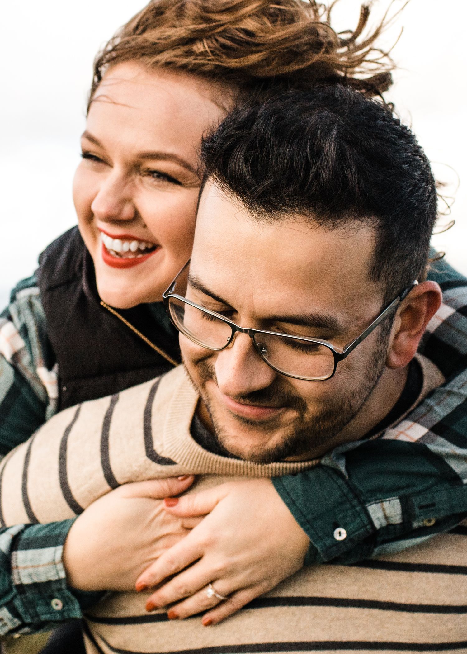 Close-up of smiling couple, woman hugging man from behind outdoors.