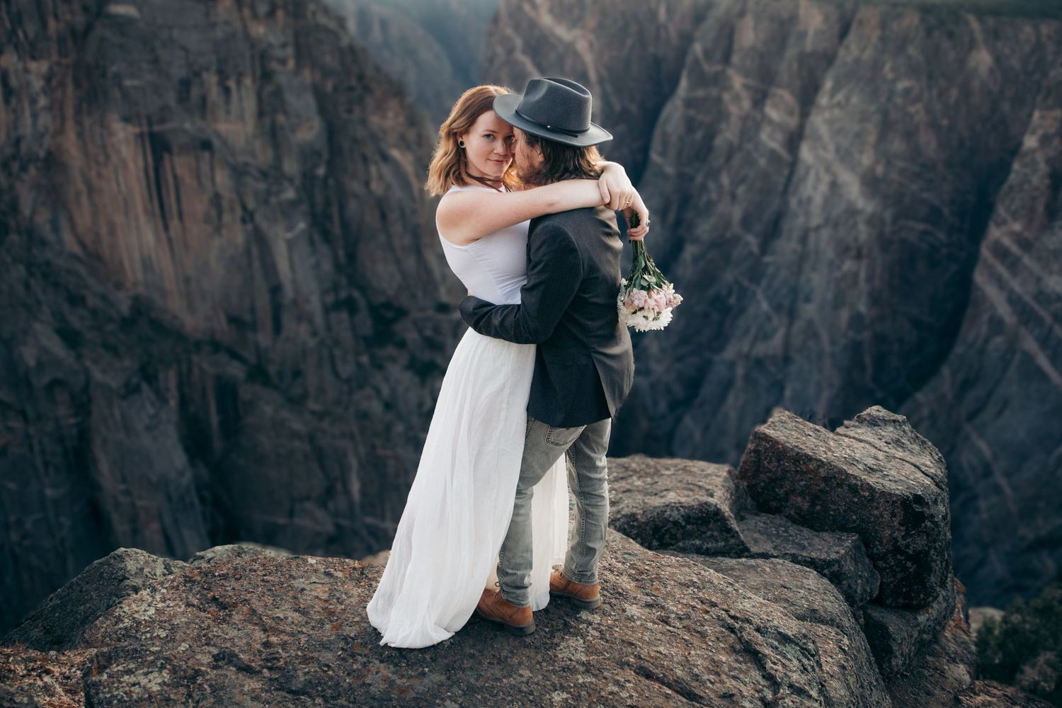 Couple hugging on rocky cliff edge with dramatic canyon backdrop.