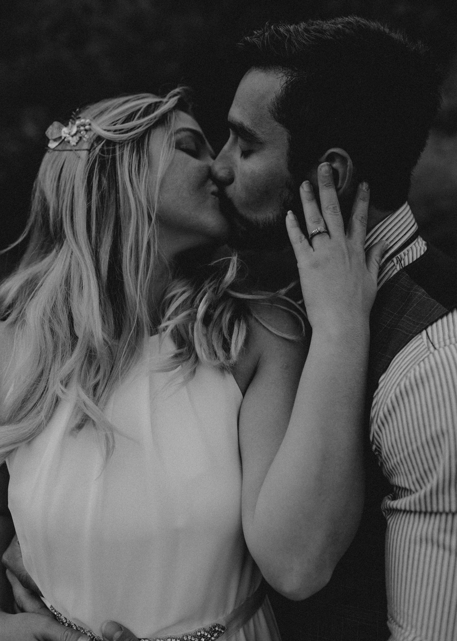 Black and white intimate photo of blonde bride and groom kissing with engagement ring visible.