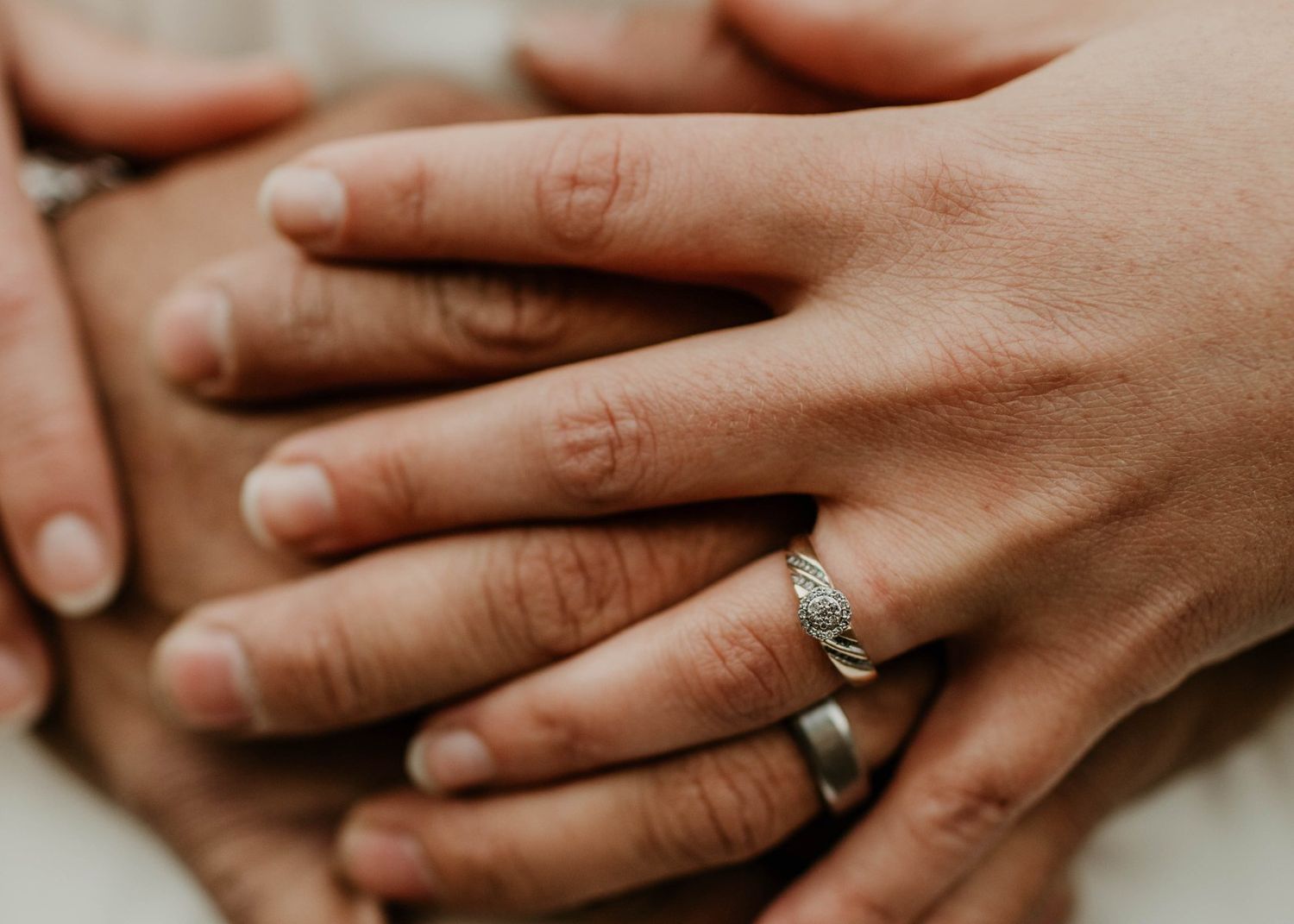 Close-up of couple's hands stacked together showing wedding and engagement rings.