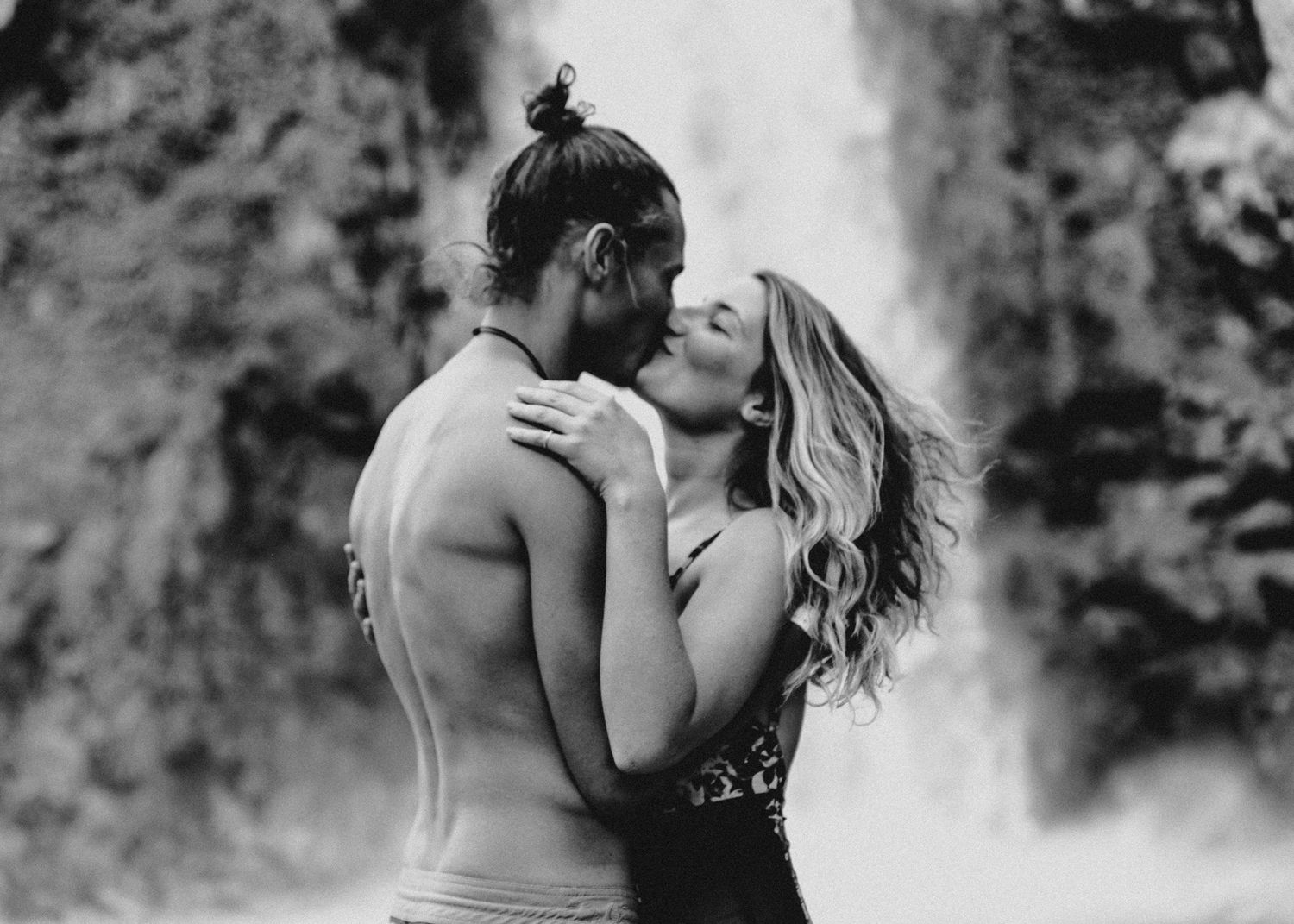 Black and white photo of a couple sharing a passionate kiss in front of a waterfall.