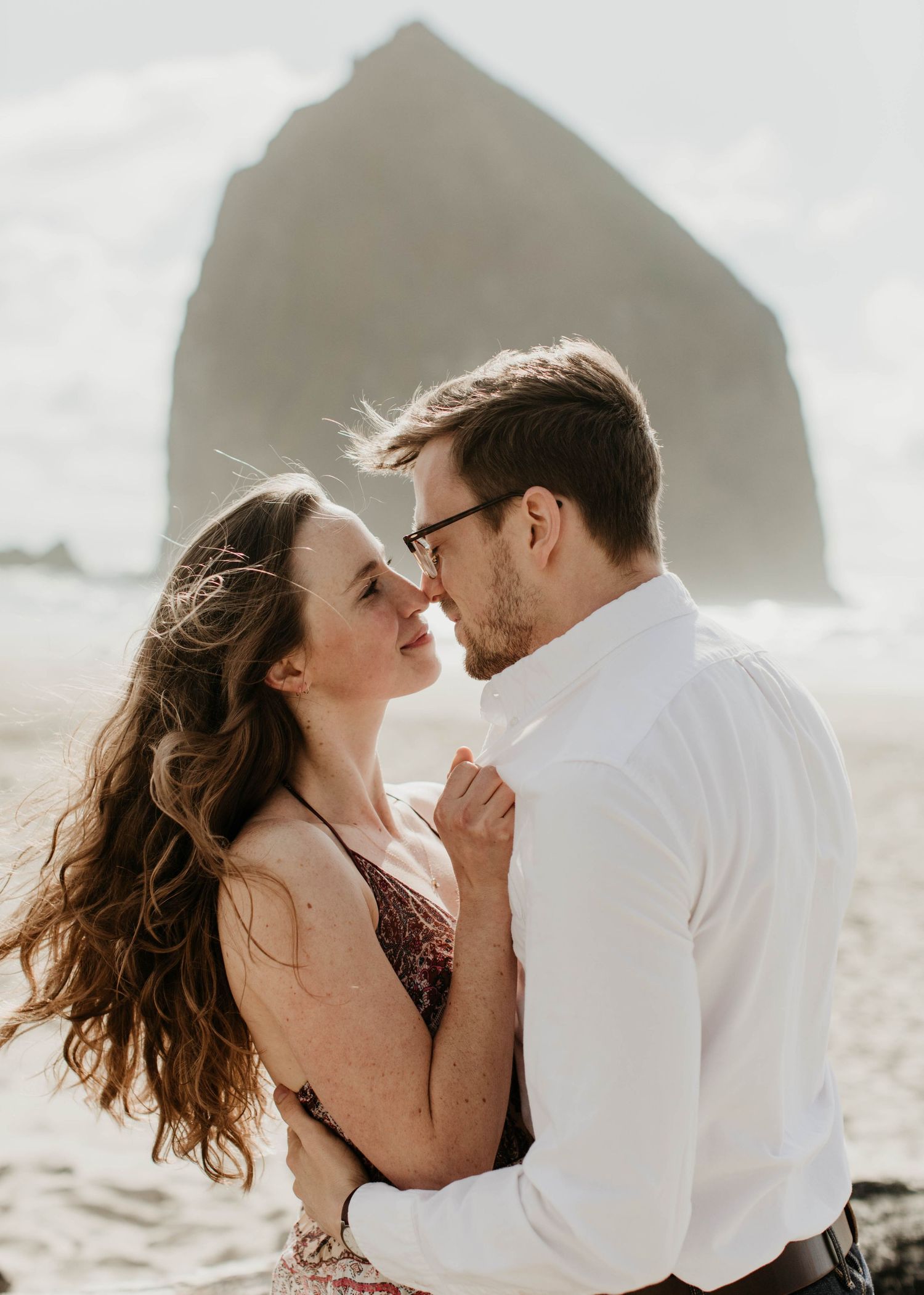 Couple sharing a romantic kiss on a beach with iconic Haystack Rock at Cannon Beach.