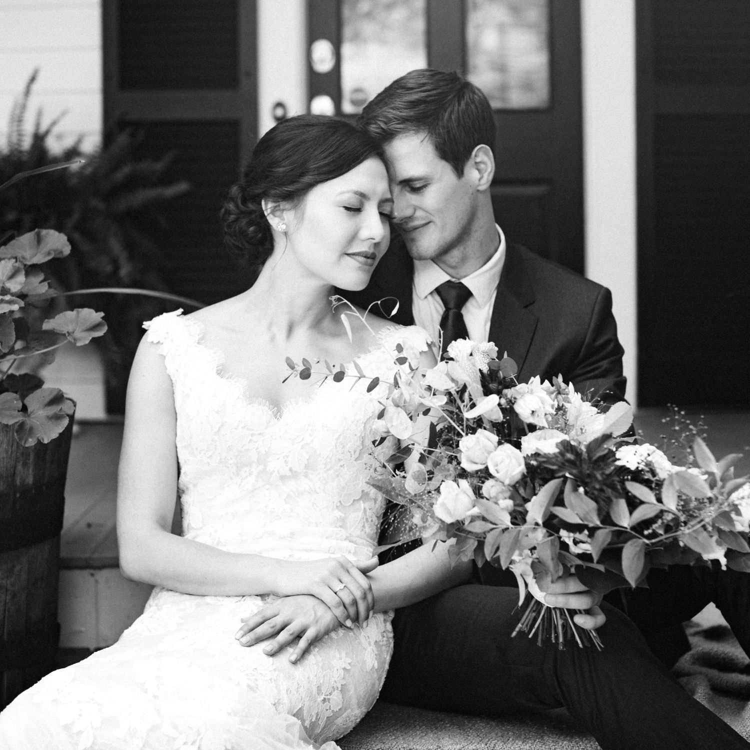 Black and white romantic portrait of bride and groom sitting on steps with bouquet.