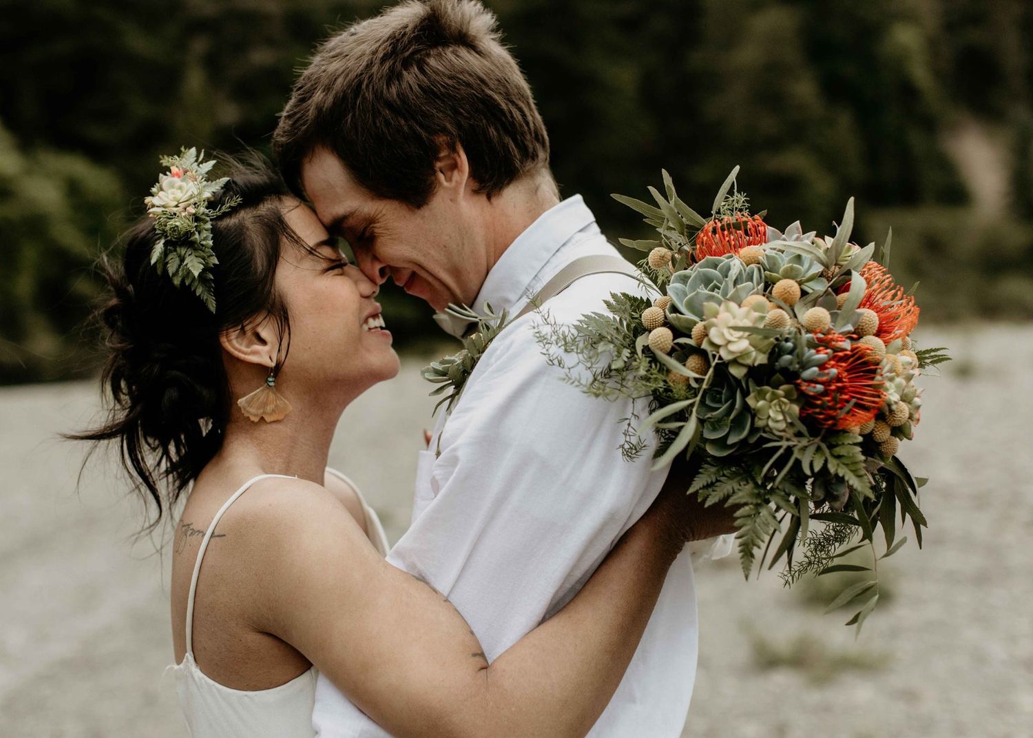 Smiling bride and groom nearly kissing, bride wearing flower crown and groom holding colorful bouquet.