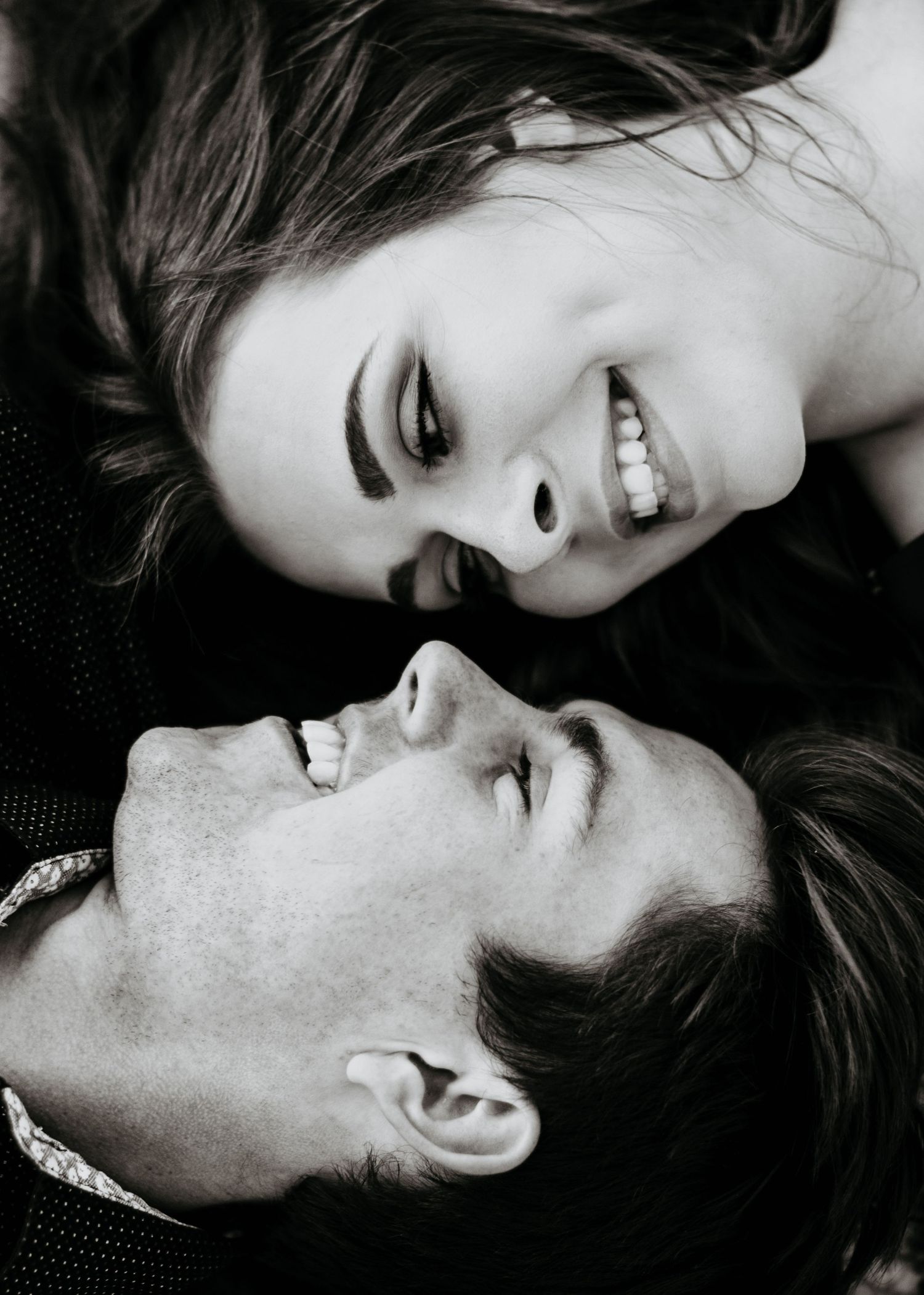 Black and white close-up portrait of smiling couple lying down face to face laughing together.
