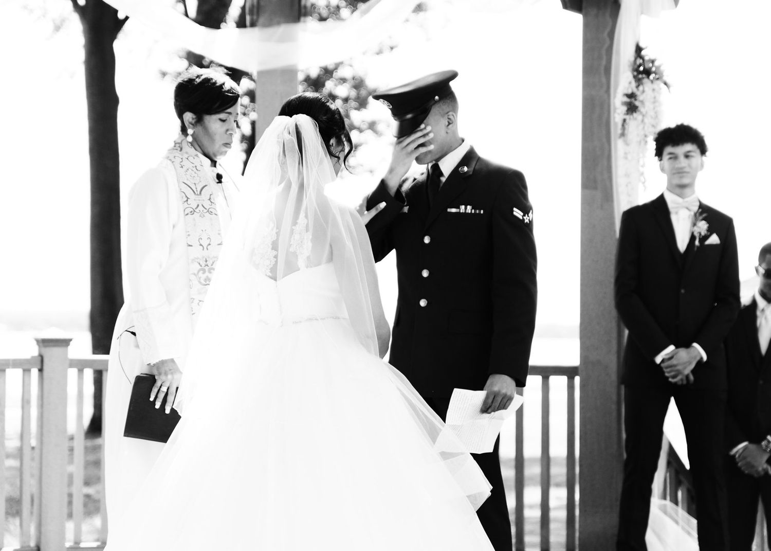 Black and white photo of military groom lifting bride's veil during outdoor wedding ceremony.