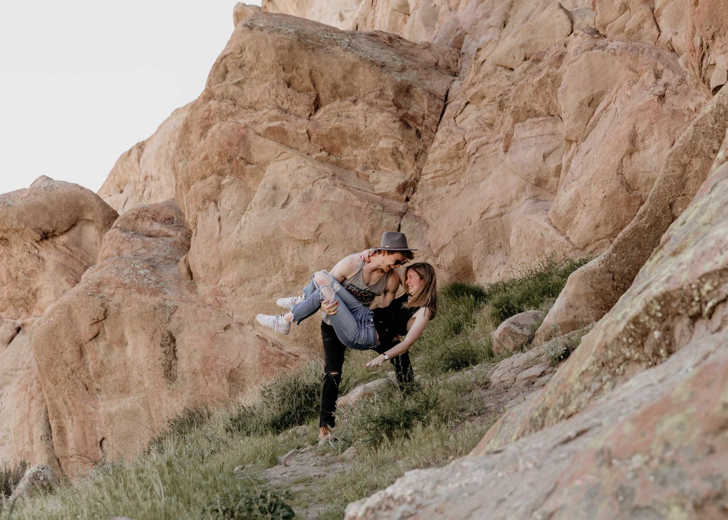 Playful couple posing on rocky desert terrain, man dipping woman dramatically on a hillside.