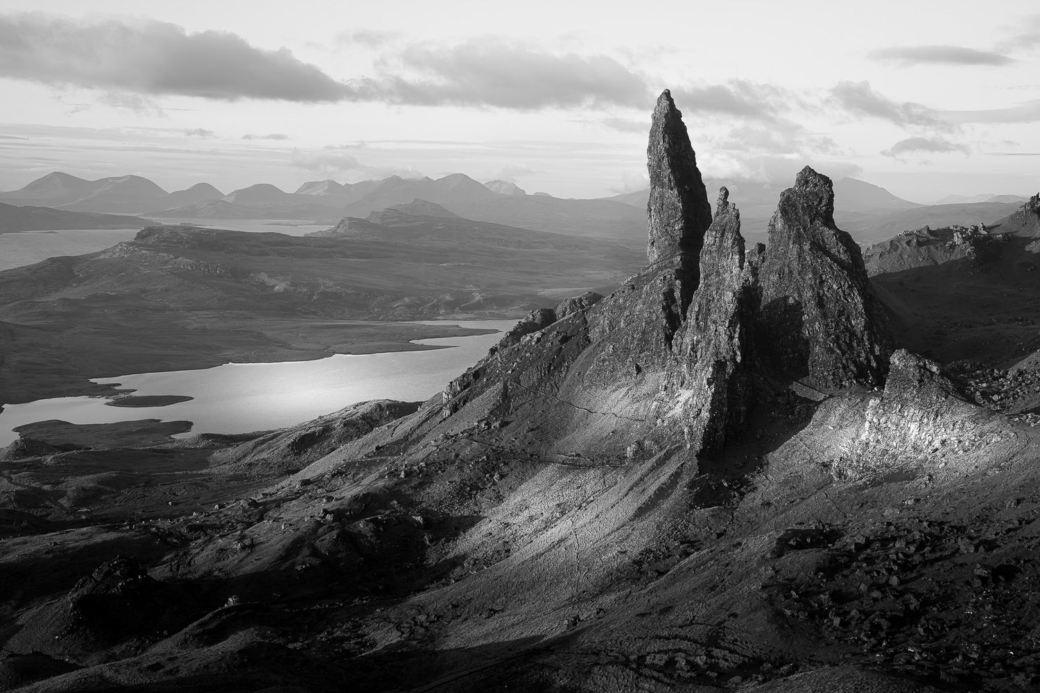 Black and white landscape of the Old Man of Storr rock formations on Isle of Skye, Scotland, with dramatic cloudy skies.