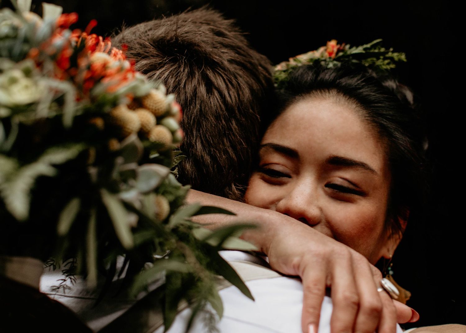 Joyful bride with flower crown hugging groom tightly, smiling warmly during outdoor wedding ceremony.