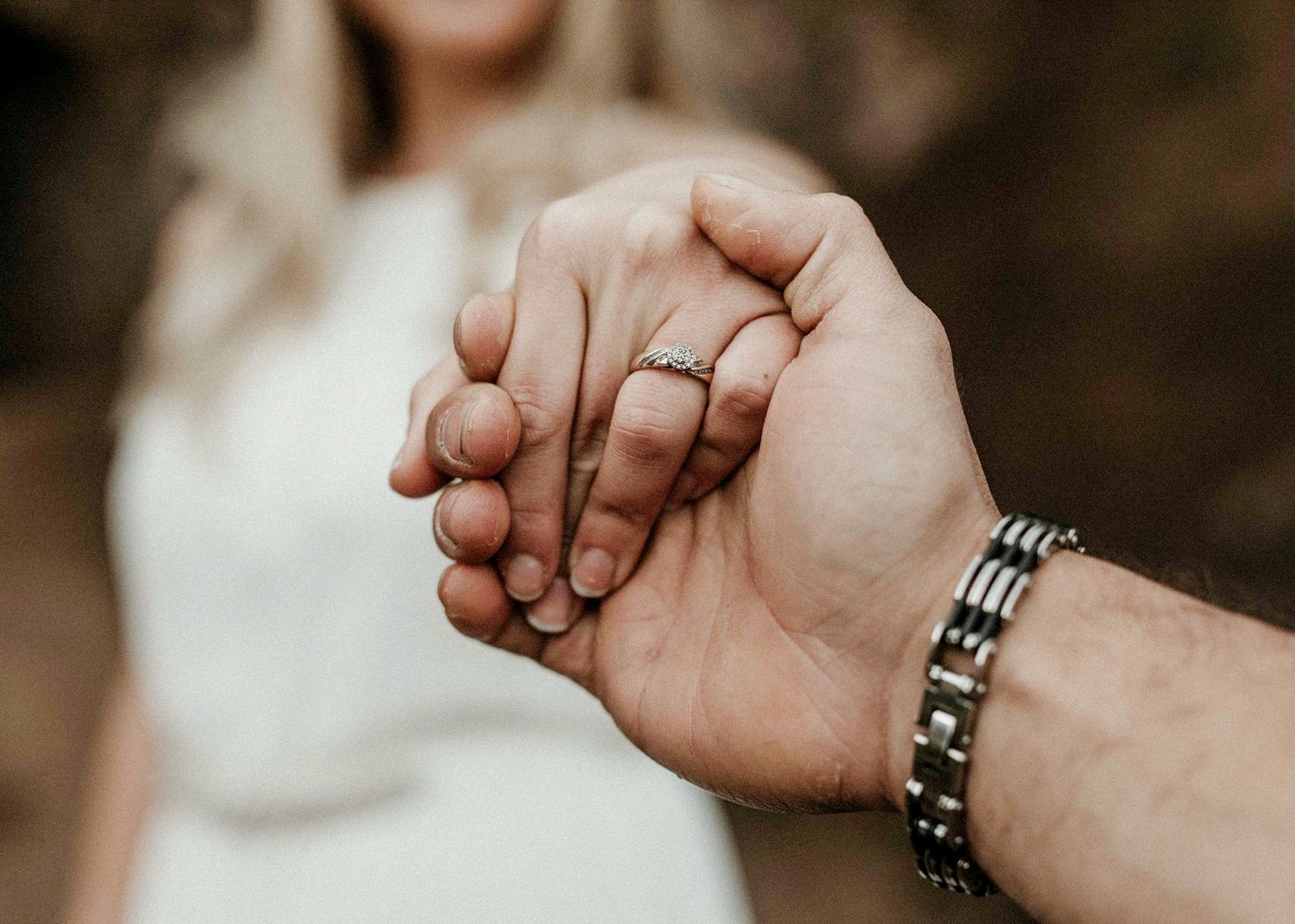 Close-up of couple holding hands showing engagement ring and silver bracelet during engagement session.