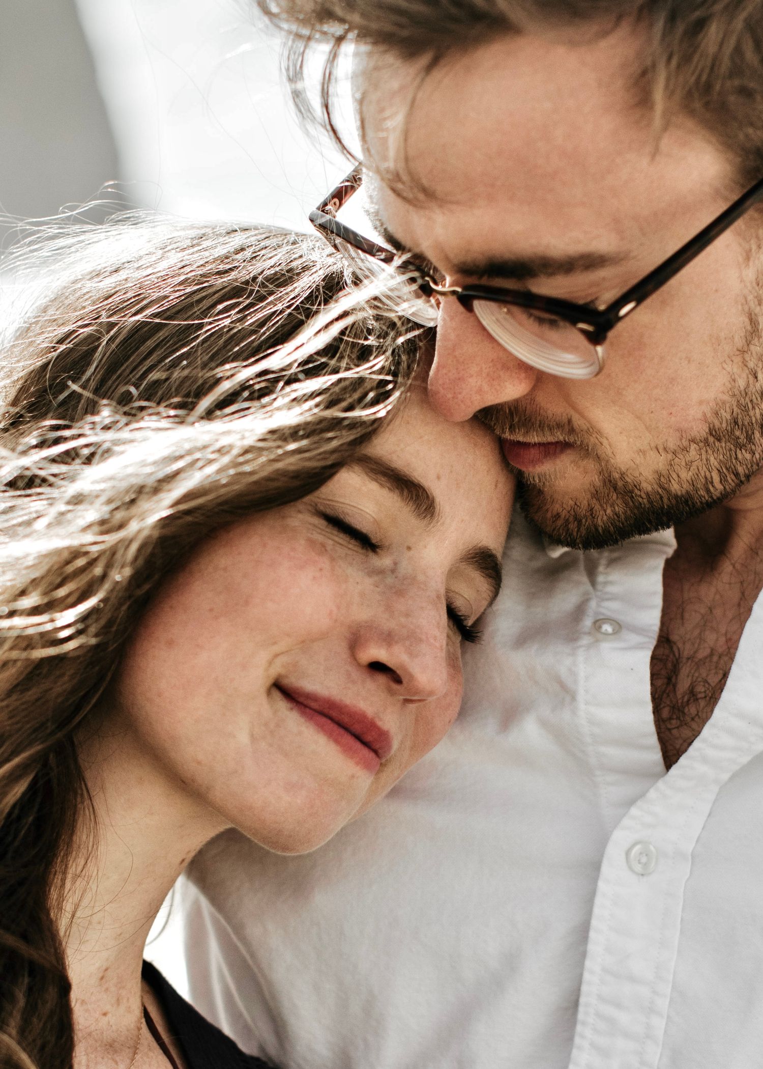 Romantic couple sharing a tender moment, man with glasses gently kissing woman's forehead.