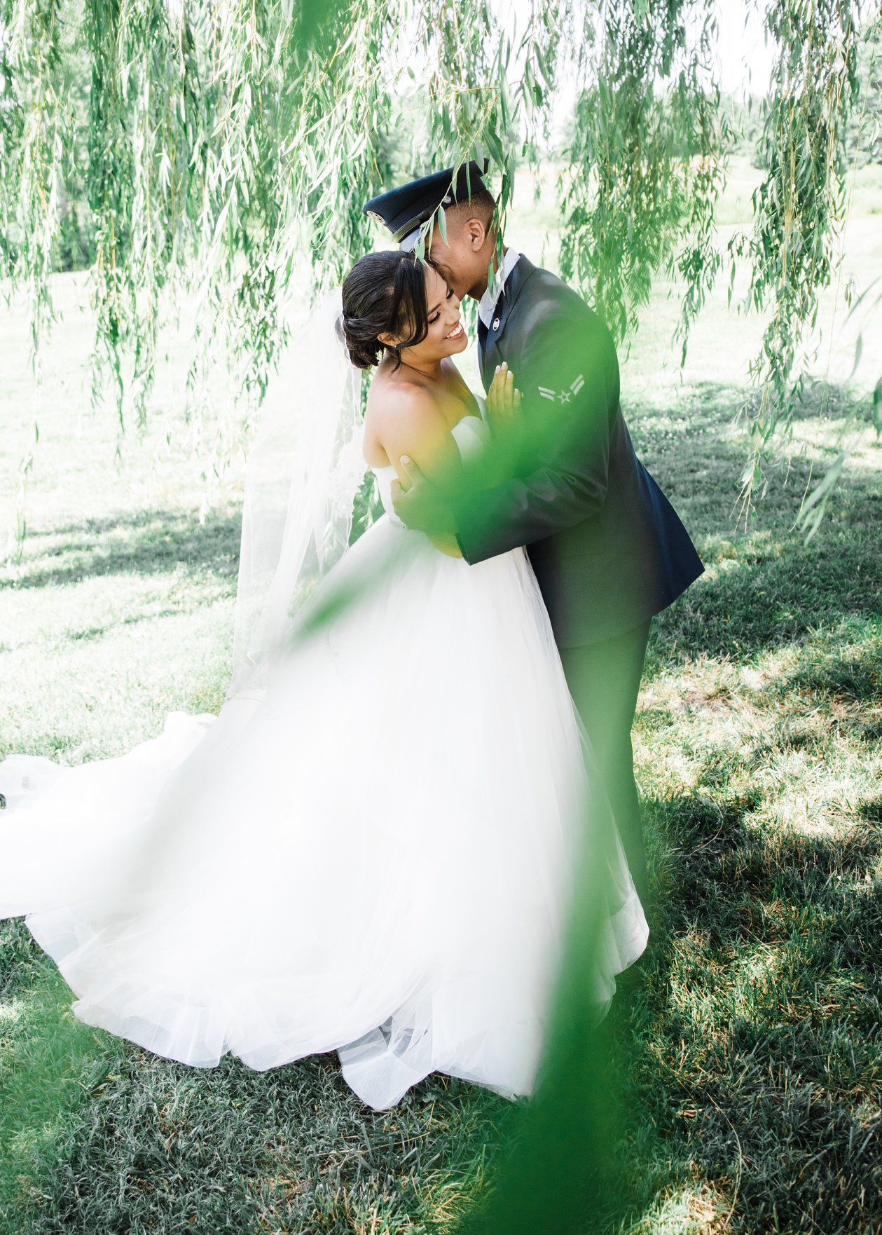 Bride and groom share romantic kiss under weeping willow tree on their wedding day.