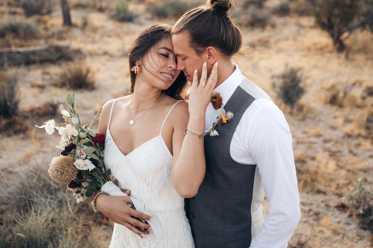 Bride and groom sharing intimate moment in arid desert setting, bride holding wildflower bouquet.