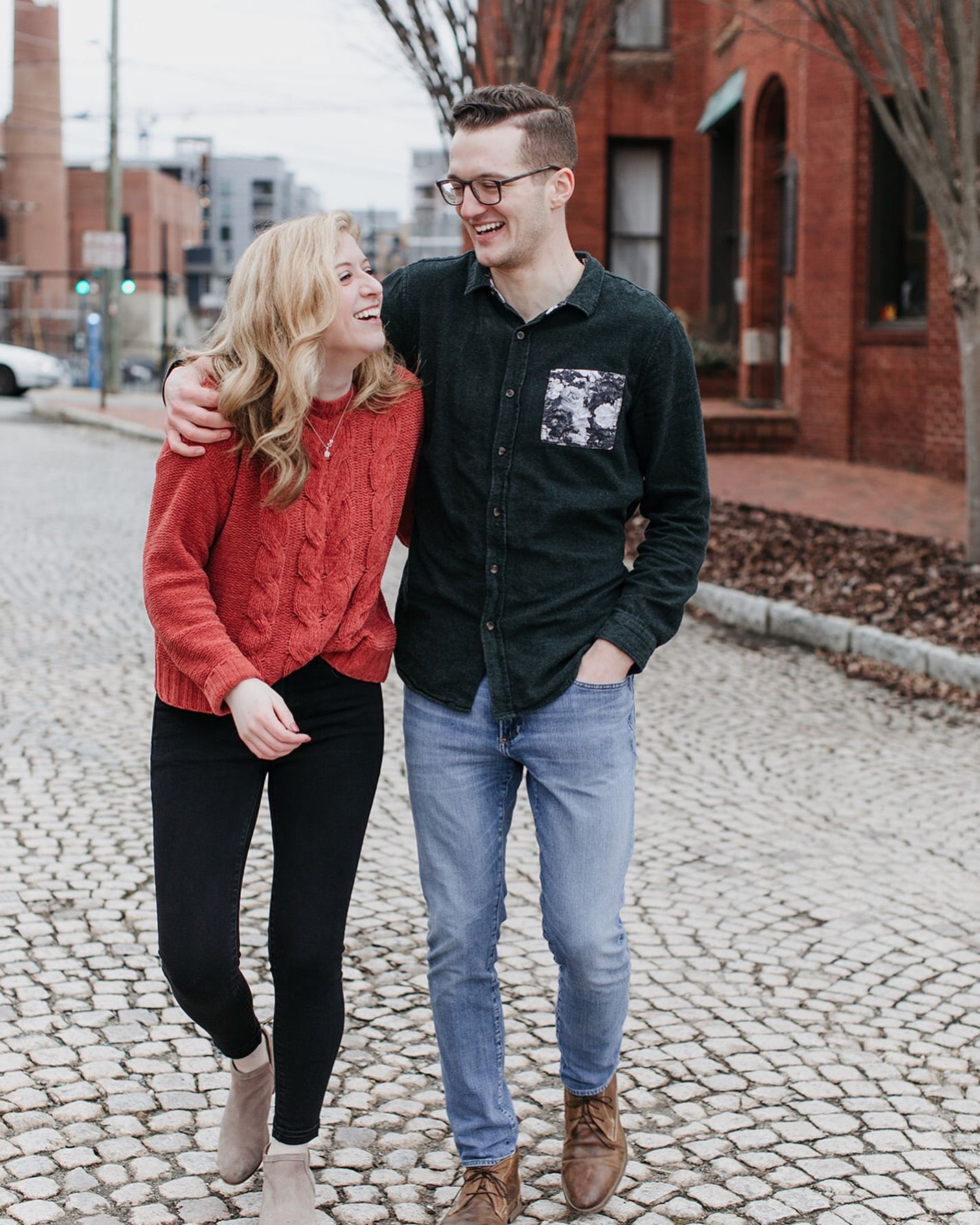 Smiling couple walking arm in arm down a charming cobblestone street in a city neighborhood.