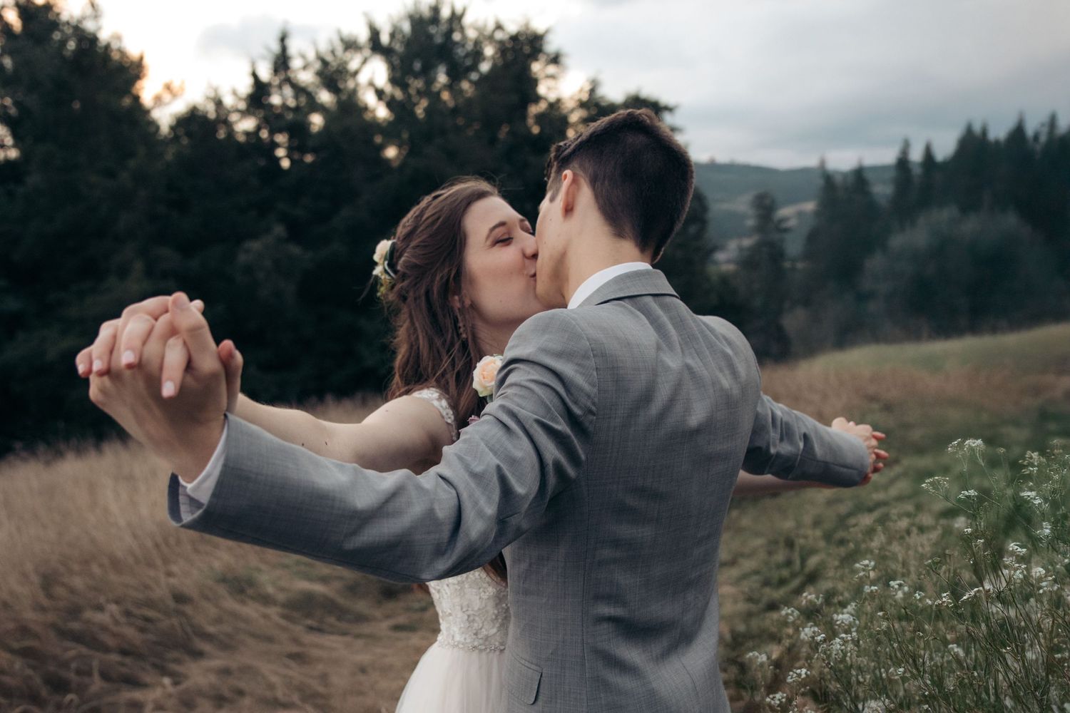 Bride and groom share a romantic kiss while dancing in a scenic mountain meadow during golden hour.