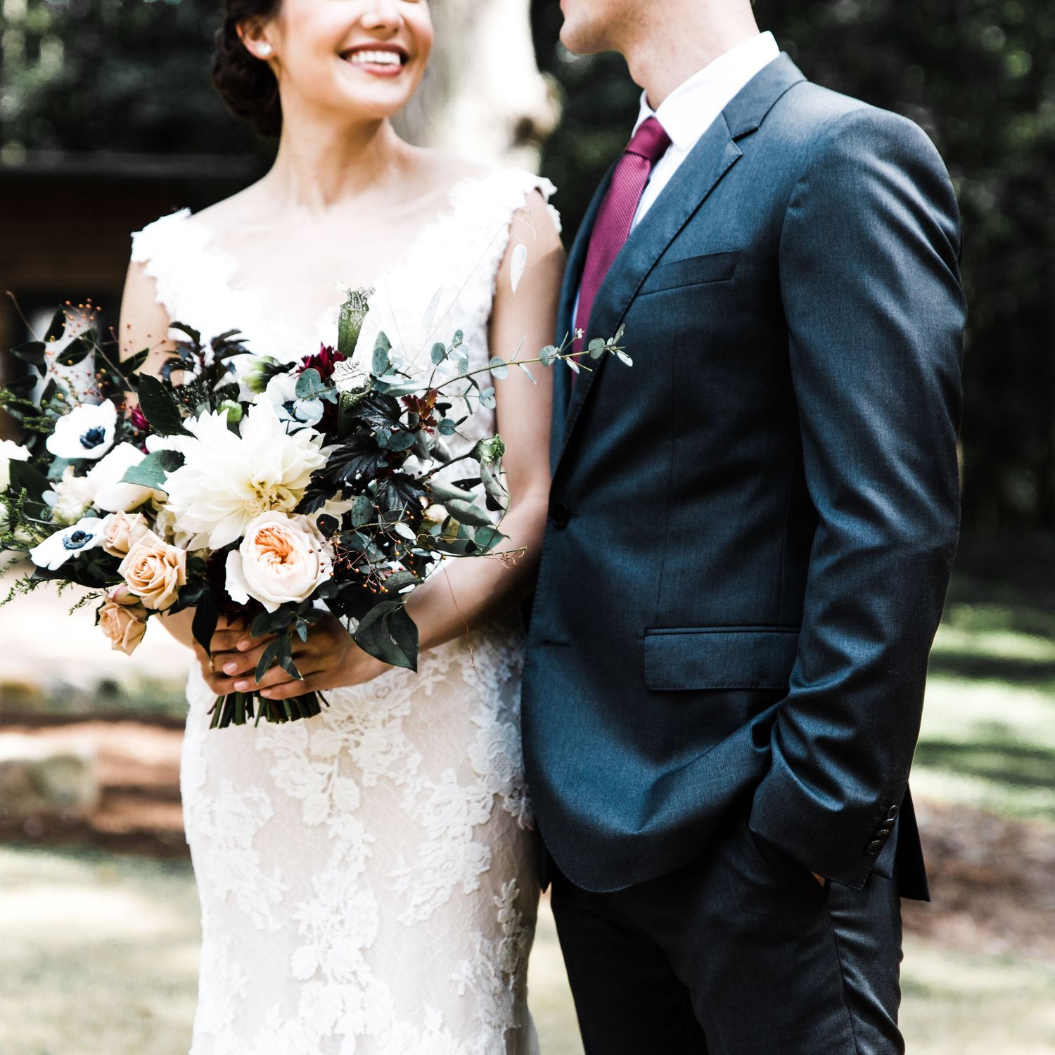 Bride and groom walking together outdoors, bride holding lush floral bouquet.