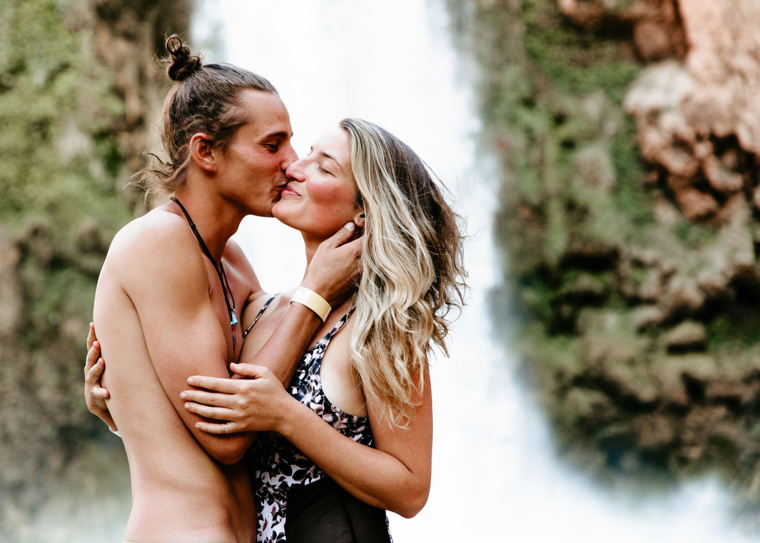 Couple sharing a romantic kiss in front of a stunning waterfall in a lush natural setting.