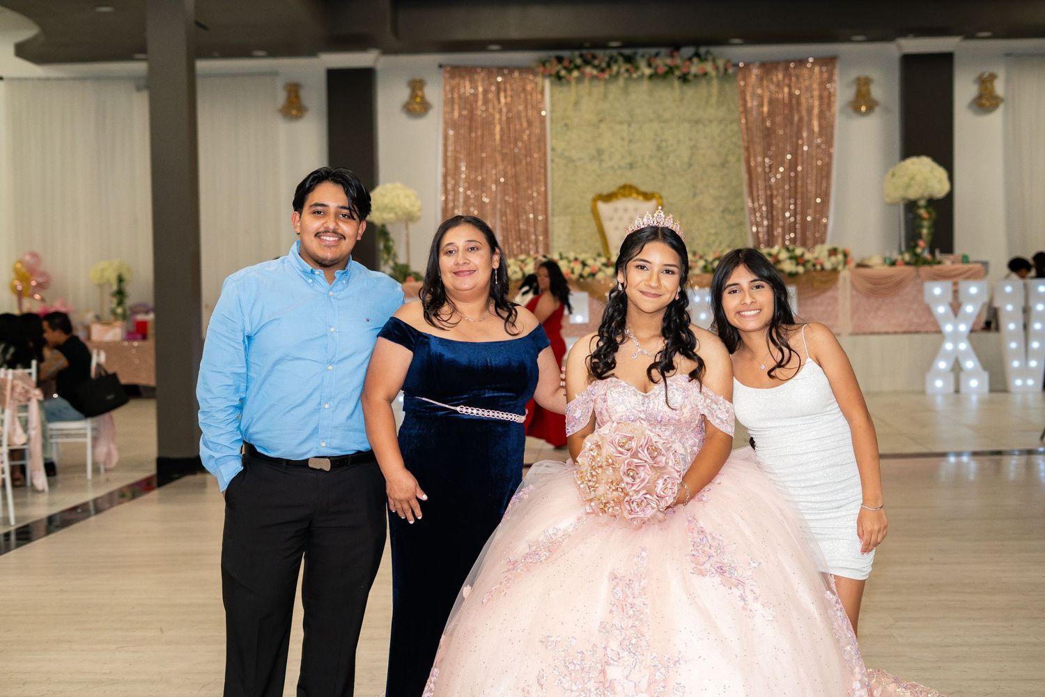 Quinceañera girl in pink ball gown poses with three family members on the decorated dance floor.