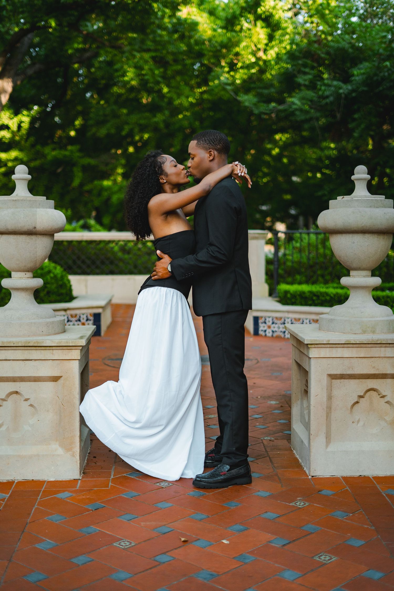 Elegant Black couple embracing romantically in formal attire at a garden venue.