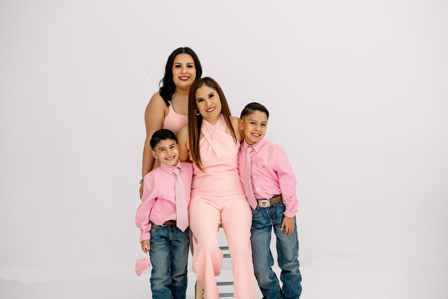 Two women and two boys in pink coordinated outfits pose in a studio.
