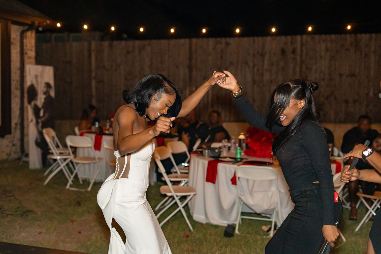 Bride in white gown dances energetically with guest at outdoor wedding reception at night.