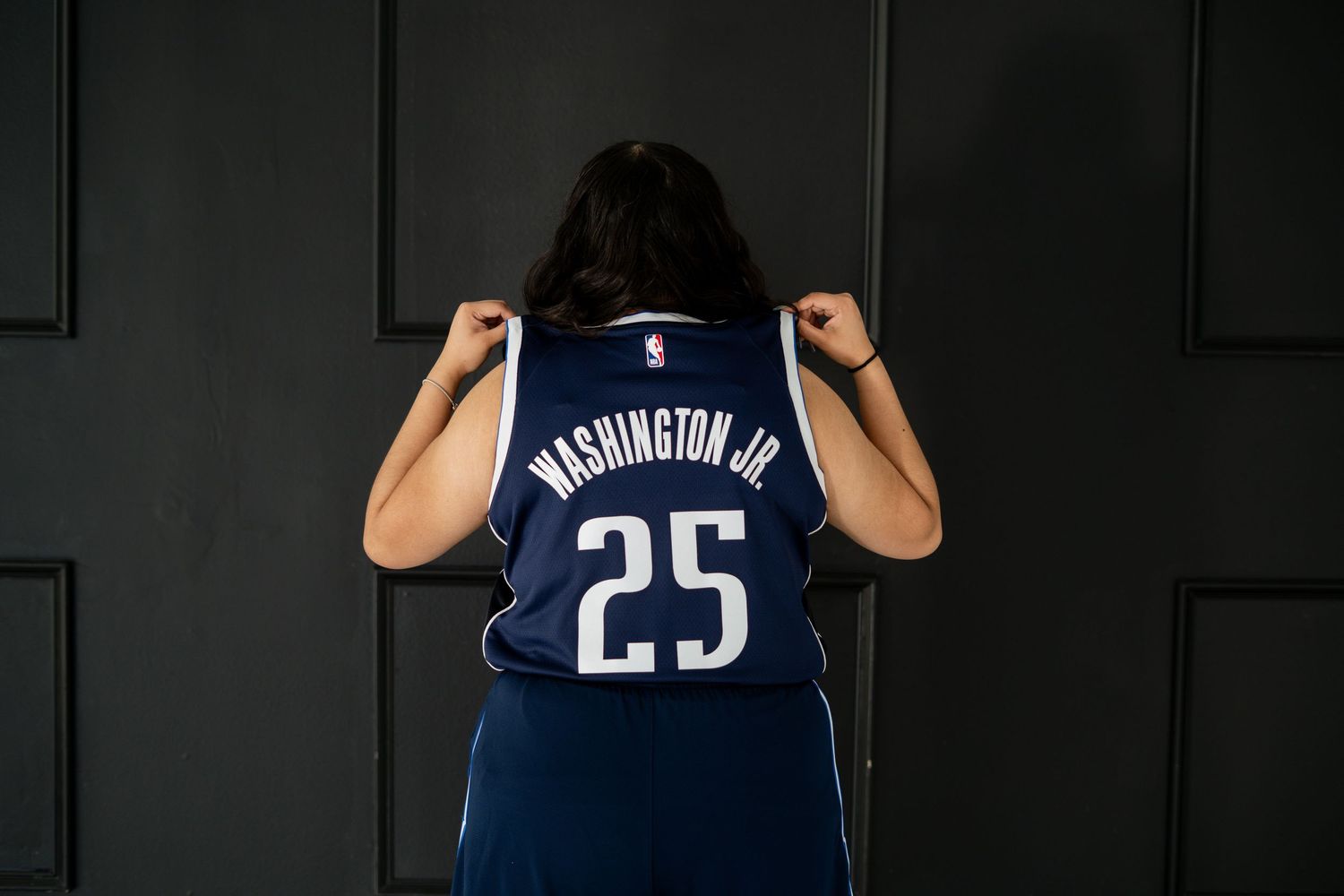 Rear view of person holding up Washington Jr. number 25 Mavericks jersey in studio.