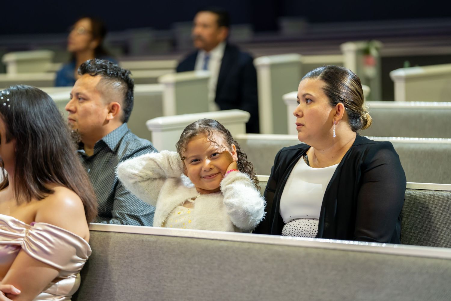 Family members including a young girl seated in church pews watching a quinceañera ceremony.