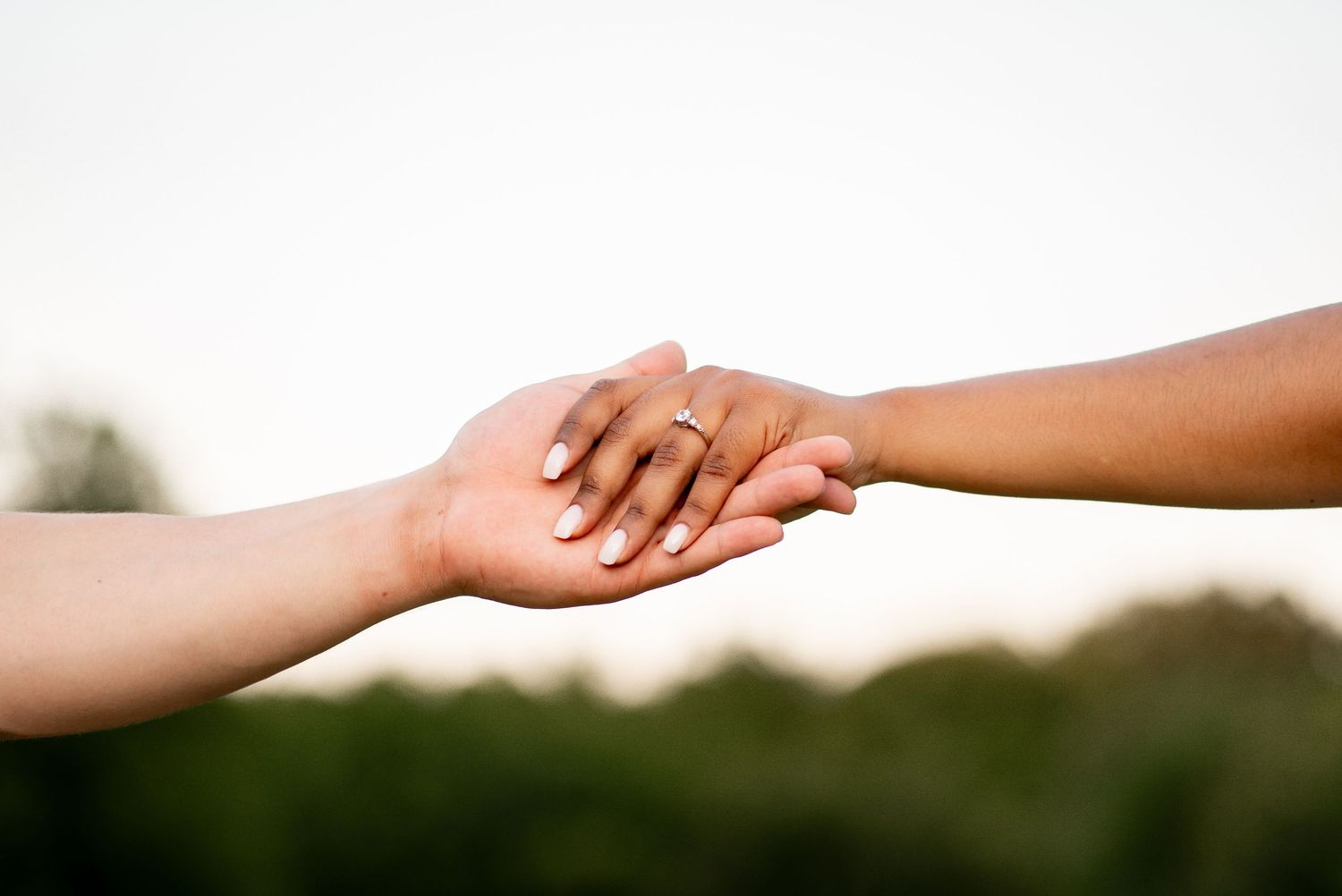 Two hands of different skin tones gently holding each other against a soft green and white background.