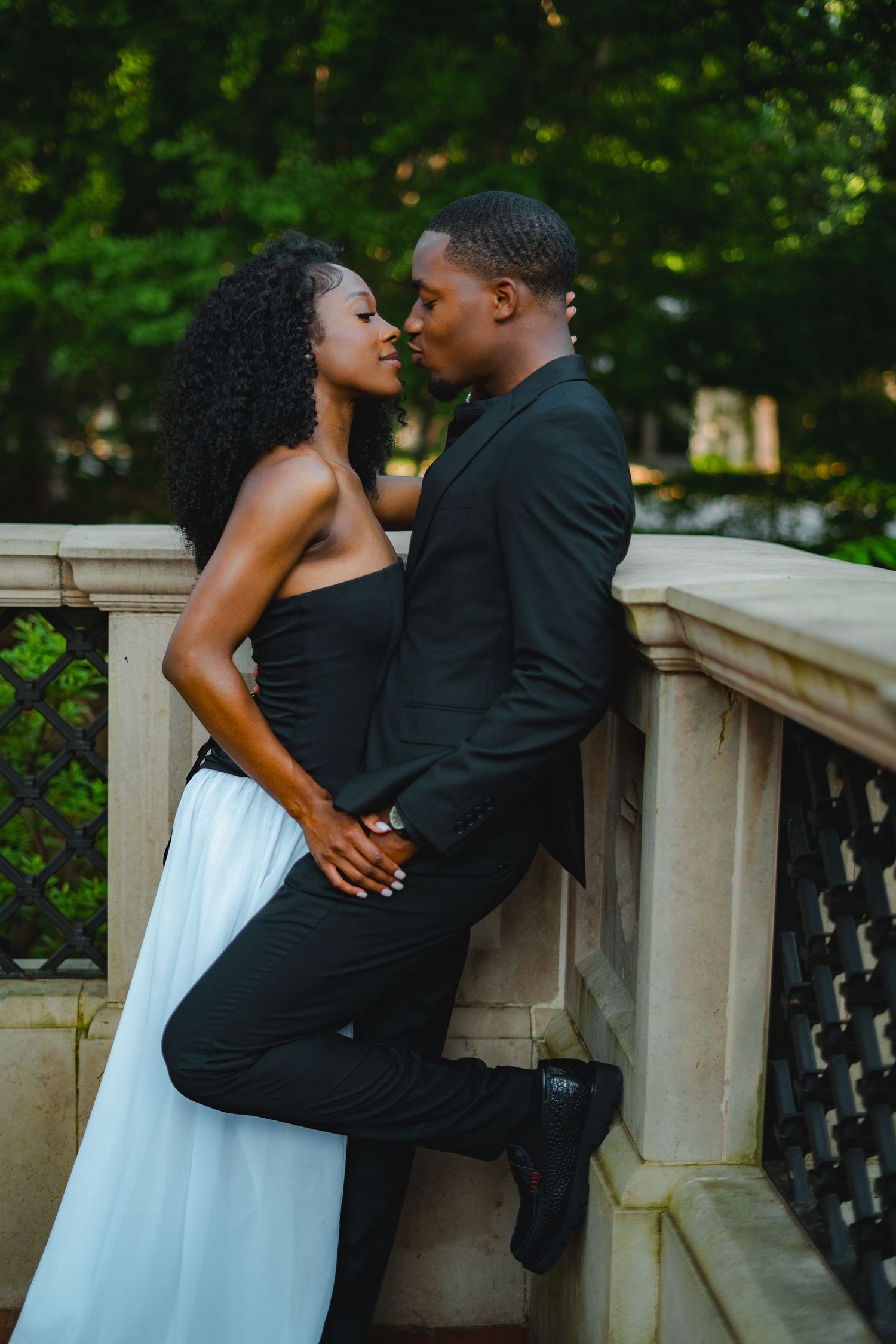 Romantic Black couple sharing a near-kiss moment leaning against stone balustrade.