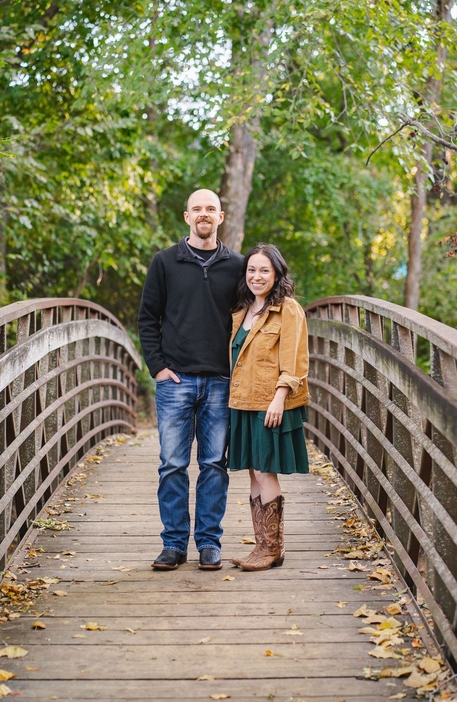 Couple standing together on a wooden bridge surrounded by fall foliage in a nature park.
