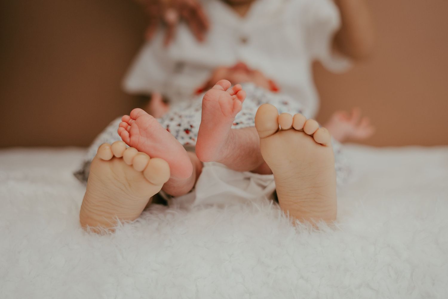 Close-up of tiny newborn baby feet beside older childs feet on a soft white fur blanket.