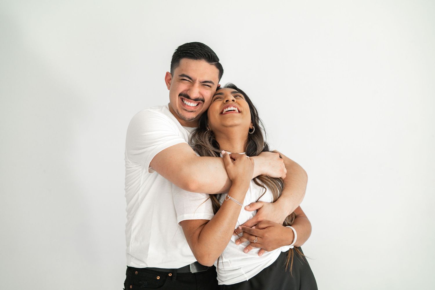 Joyful couple hugging and laughing together against a clean white studio background.