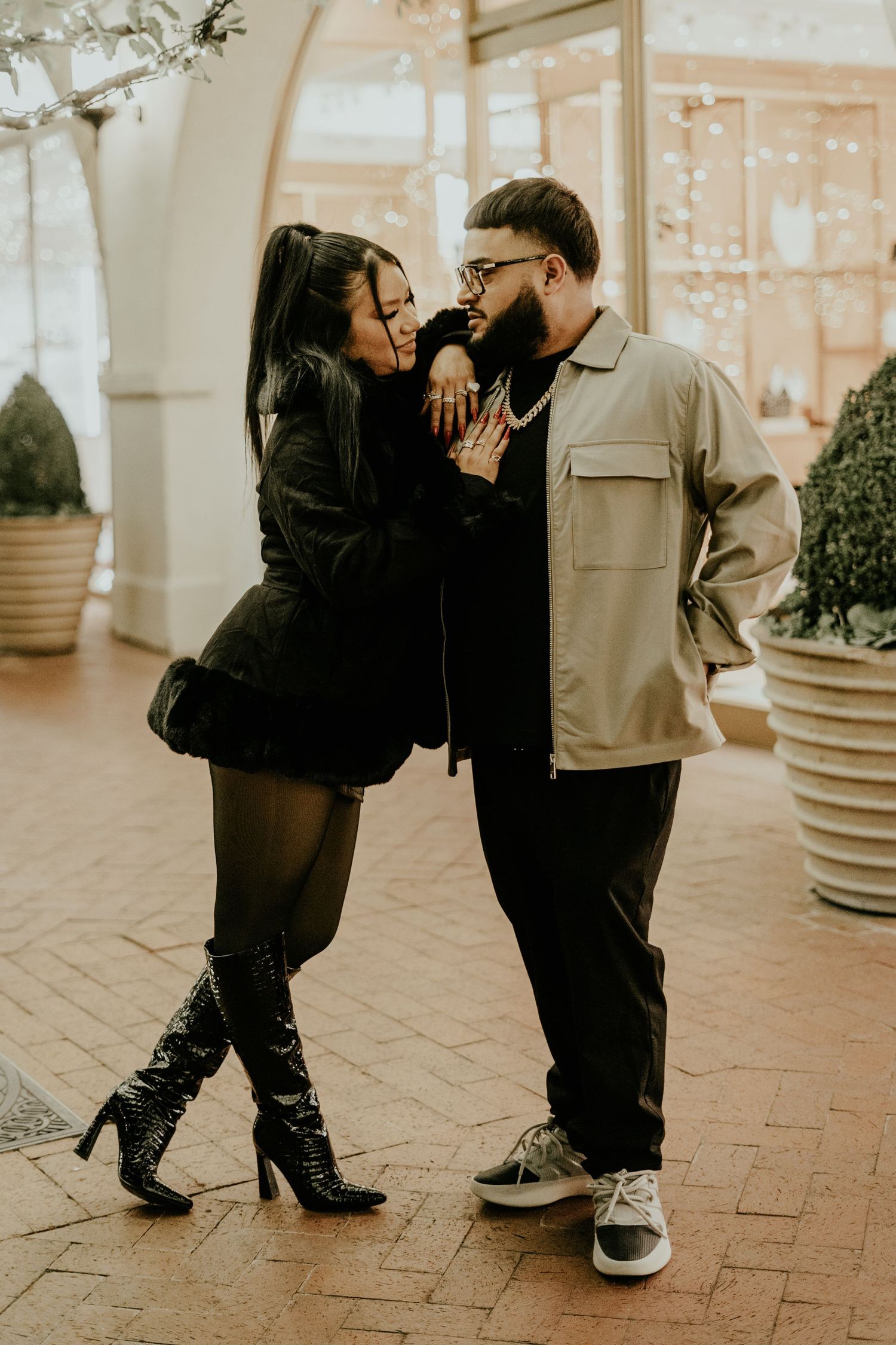 A couple shares a romantic moment on a brick walkway, woman in black outfit and knee-high boots.